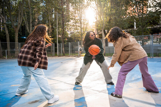 Gen-Z women friends playing basketball on sunny court