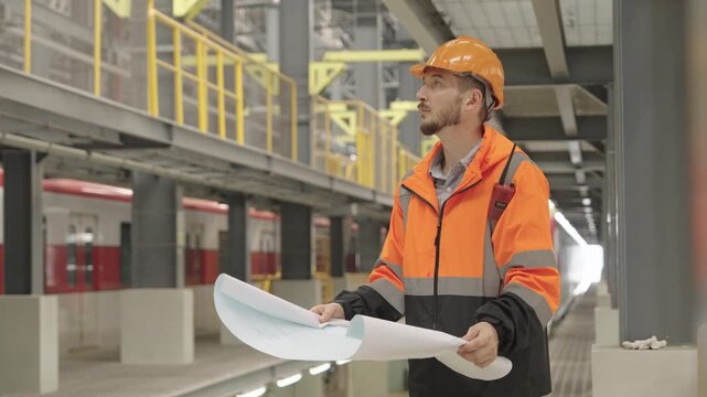 Architect intently examines detailed architectural plans within dimly lit construction hallway featuring metal support beams and bright white illumination for precise design assessment.