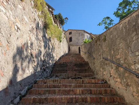 Scalinata ripida in mattoni tra antiche mura in pietra, immersa in un borgo storico con vista su una casa in pietra e cielo limpido