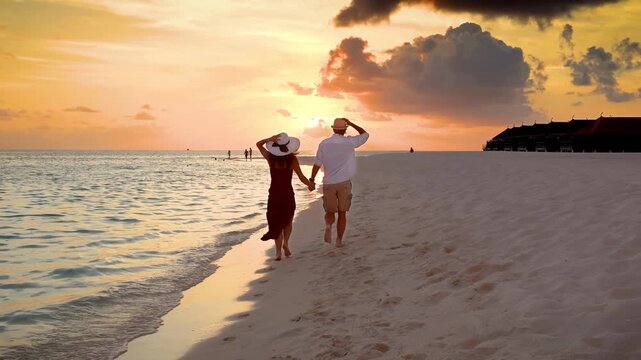 Slow motion view of a beautiful couple holding hands and running down a tropical beach during sunset time in the Maldives islands