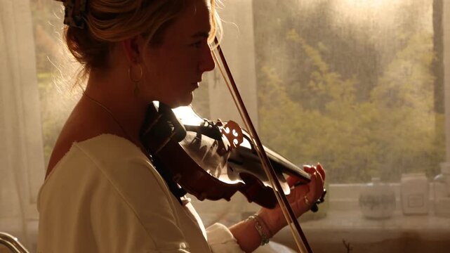 young woman playing violin in bathroom at sunset