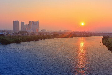 Fototapeta premium Sunset over the river with city skyscrapers and sun flare