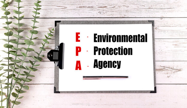 Epa environmental protection agency acronym on clipboard with pen and green foliage on wooden background representing environmental