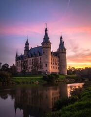 Fototapeta premium Historic castle illuminated by vibrant sunset sky reflected in tranquil water