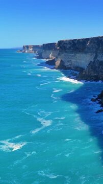 4K vertical drone footage approaching Australia&rsquo;s Bunda Cliffs from offshore, showing blue sea, white surf, and layered vertical cliffs
