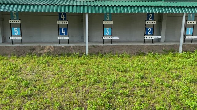 An outdoor shooting range with numbered targets and lanes, with a metal-roofed, grass-covered practice range in the foreground