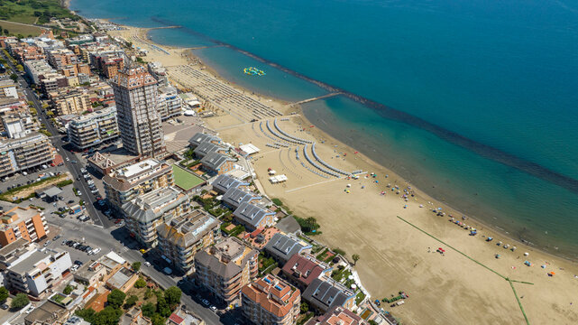 Aerial view of Nettuno coastline featuring the iconic skyscraper, sandy Scacciapensieri beach with umbrellas, seaside residential buildings, and the Mediterranean sea. It Is located in Lazio, Italy.