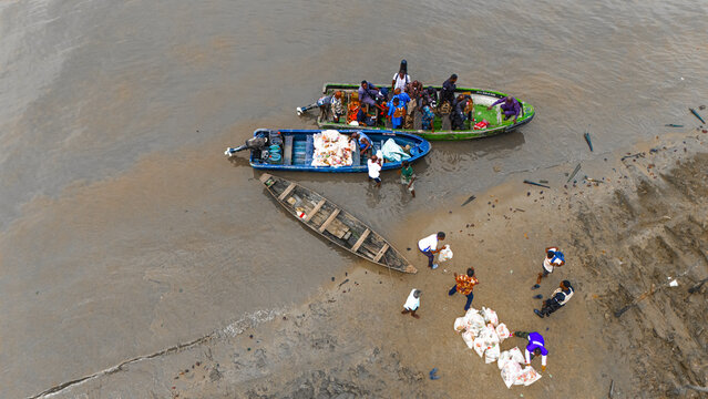 Aerial view of people unloading goods from small boats onto a muddy riverbank in Minima, Rivers, Nigeria.