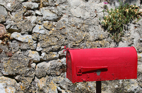 Red vintage mailbox against an old rustic stone wall in rural Italy