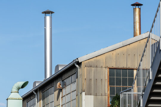 Rustic Japanese industrial factory building with rain-capped exhaust chimneys, corrugated metal siding, and multi-pane industrial windows set to a clear blue sky.