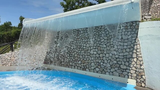 Close-up of a backyard ornamental pool waterfall with uneven and broken water flow caused by malfunctioning or weak water pumps.