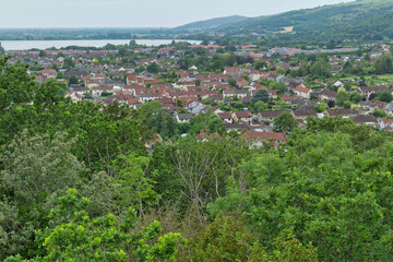 Fototapeta premium A scenic high-angle view shows a town with houses nestled among green trees. In the background, a body of water meets distant hills in Cheddar Gorge - Cheddar - Somerset - UK