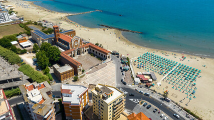 Aerial view of the sanctuary of Our Lady of Grace and Saint Maria Goretti, in Nettuno, Lazio, Italy. It stands at the end of the seafront, along the coast, next to a sandy beach lined with umbrellas. © Stefano Tammaro