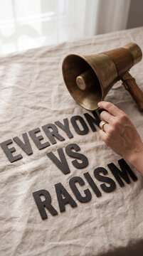 Close up of a hand holding a vintage brass megaphone on a textured fabric cloth printed with the text everyone vs racism