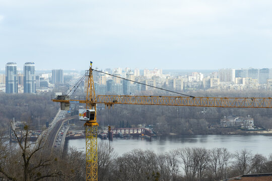 Kyiv, Ukraine - March 22, 2026: Liebherr construction crane stands over a river and city bridge, showing urban development projects across a modern metropolitan landscape horizon