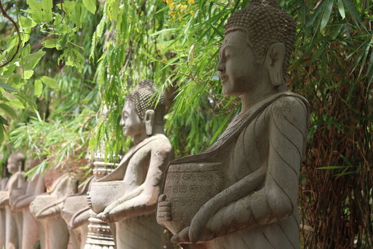 Stone Buddhist Monk Statues Holding Inscribed Bowls Among Lush Bamboo Garden at Prasat Vimean Koh Pos Kien Svay Cambodia