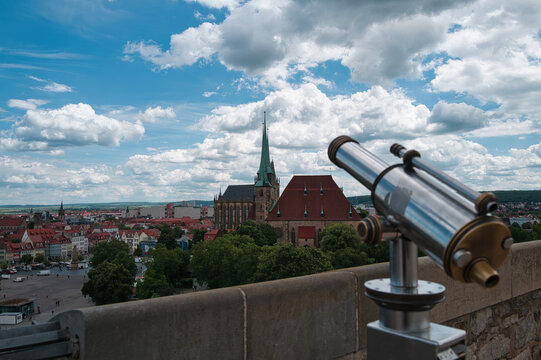 Telescope in the foreground with the cathedral in Erfurt, Germany, in cloudy weather.