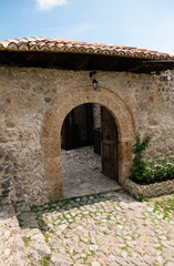 Obraz premium Historic stone arch entrance with rustic wooden door in medieval architecture courtyard.
