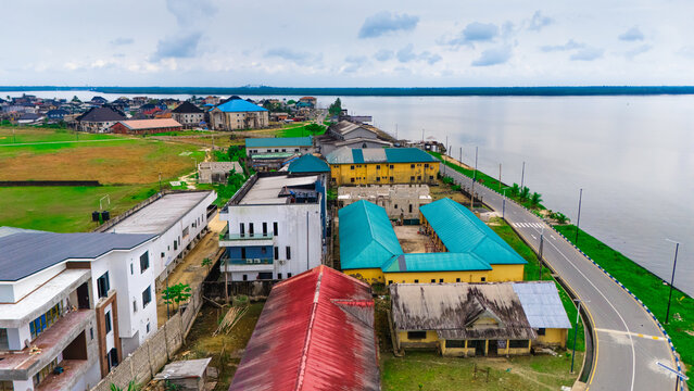 Aerial view of a coastal town in Rivers, Nigeria, featuring residential buildings with colorful roofs, a paved road running along the water, and lush green spaces.
