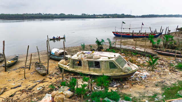 Aerial view of a riverbank featuring several small wooden boats, a weathered cabin boat, and people in a canoe on the water in Minima, Rivers, Nigeria.