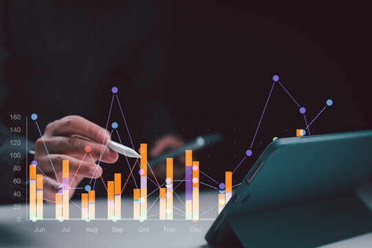 Male hand uses pen point bar chart line graph over tablet screen dark room study finance data metric late night work indoors focus year growth result report review market trend profit gain plan.