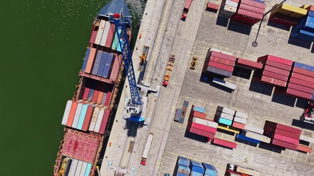 A large cargo ship sits at the dock being loaded with colorful shipping containers. Workers operate a crane to move items efficiently in the busy port.