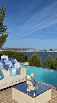 Elegant wedding lounge by an infinity pool adorned with blue and white hydrangeas overlooking the Mediterranean Sea and Marseille. Luxury outdoor reception setting in bright sunshine.