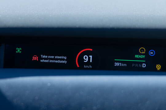 Electric car dashboard display showing speed of 91 km per h and warning message to take over steering wheel immediately in a modern vehicle interior