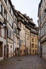 Fototapeta premium Tall historic facades forming narrow corridor, muted palette, cobblestone floor, overcast light, quiet city mood, architectural rhythm