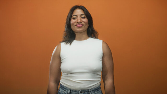 Woman pouts lips with bare shoulders wearing white sleeveless top and jeans in studio with orange backdrop, mid transition to smile across frames; playful confidence.