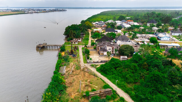 Aerial view of a riverfront settlement with houses, lush green vegetation, and a wooden pier extending into the river in Rivers, Nigeria.