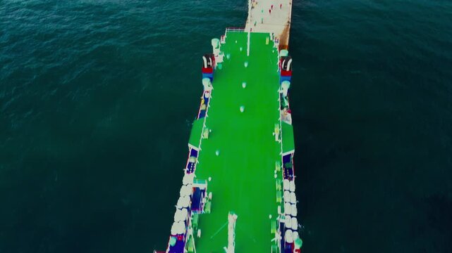 Drone view of a blue and white roll-on/roll-off ship connected to a coastal port ramp.