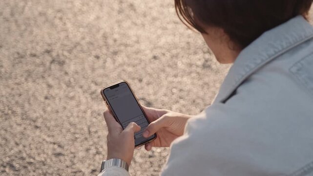 Young man outdoors  typing a text message.  Male person looks into a cell phone and types a text - outdoors, park. People and technology.  Guy is typing a text message on a mobile phone.