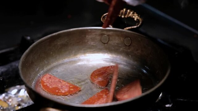 Sucuk slices are cooked in oil in a copper pan. Close-up scene showing hot breakfast food preparation, pan cooking process and appetizing sucuk detail.