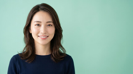 Fototapeta premium ミントグリーンの背景で微笑む女性を描いたライフスタイルイメージです。 清潔感のある表情が美容や健康、ビジネスシーンにも活用しやすい印象を与えます。