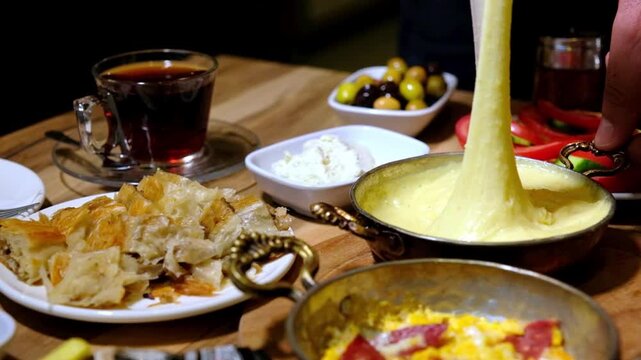Traditional Turkish breakfast presentation with kuymak and sucuklu eggs. A rich breakfast table with tomatoes, cucumbers, cheese, and olives is shown in close-up.
