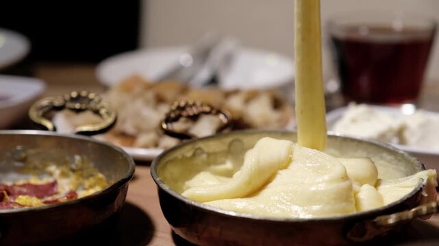 Traditional Turkish breakfast presentation with kuymak and sucuklu eggs. A rich breakfast table with tomatoes, cucumbers, cheese, and olives is shown in close-up.