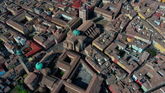 Top-down drone view of Parma Cathedral, Baptistery, and Piazza Duomo amid terracotta rooftops in Parma, Emilia-Romagna, Italy, daytime.