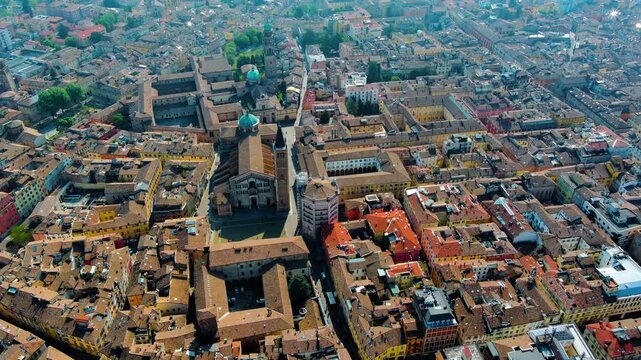 Aerial drone panorama of Parma's old town featuring Parma Cathedral, Baptistery, and Strada Duomo amid rooftops, Emilia-Romagna, Italy, daytime haze.
