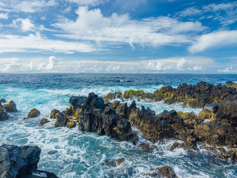 Powerful white ocean waves foaming and crashing into dark volcanic rock reefs near Porto Moniz natural pools, Madeira, Portugal.
