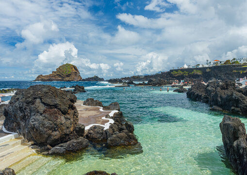 Crystal clear turquoise water inside the natural volcanic rock swimming pools under a bright blue sky in Porto Moniz, Madeira, Portugal.