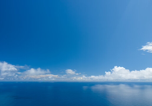 A vast landscape view of the deep blue Atlantic Ocean meeting the horizon under a wide sky with wispy clouds, Madeira, Portugal.