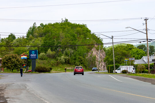 Gaspesie, Quebec, 06 June 2026 : A red SUV drives on a road past a Clarion Pointe hotel sign, with a man walking and a cyclist.