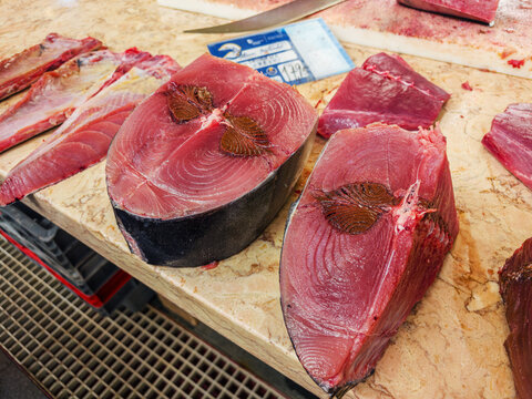 Large fresh raw red tuna fish steaks displayed on a wooden table at a traditional seafood market, Funchal, Madeira, Portugal.