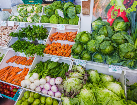 A wide market display of fresh green vegetables including broccoli, leeks, lettuce, and cabbage on a shelf.
