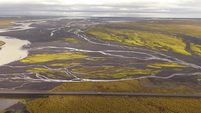 Aerial view of a car driving along the Ring Road crossing a wide plain of braided glacial rivers flowing from Vatnajokull glacier in Iceland