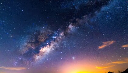 Fototapeta premium The majestic Milky Way galaxy stretches across a vibrant night sky, illuminated by countless stars and distant nebulae, with a soft orange glow on the horizon.