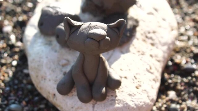 Clay sculpture hands, person shaping raw clay into small animal figure on sunny pebble beach