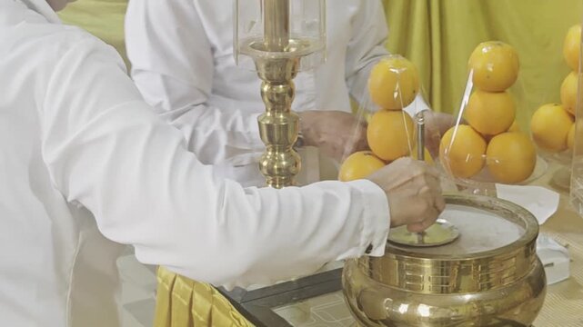 a person in a clean white uniform using a metal tool to smooth down the ash inside a ceremonial brass incense burner vessel