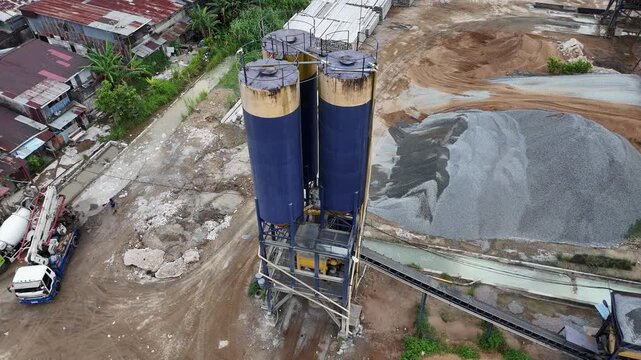 An aerial view of a concrete plant&rsquo;s silo tower and piles of gravel at a building materials storage yard.